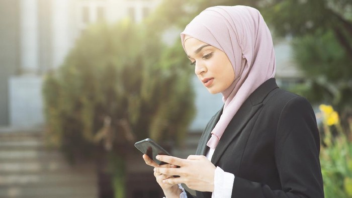 Muslim business woman walking and using smart phone.