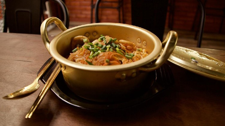 Ramyeon, a Korean style noodles in golden pot on the wooden table