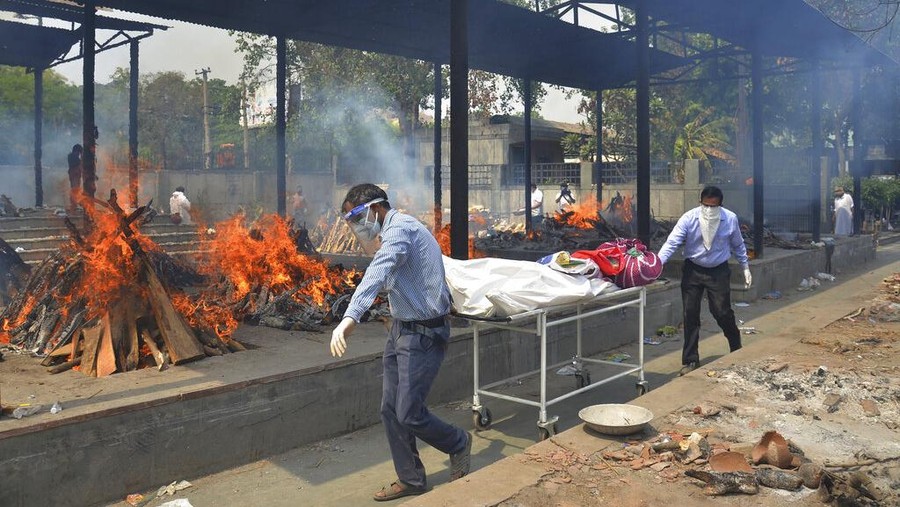 FILE - In this May 1, 2021, file photo, relatives carry the body of a person who died of COVID-19 as multiple pyres of other COVID-19 victims burn at a crematorium in New Delhi, India. COVID-19 infections and deaths are mounting with alarming speed in India with no end in sight to the crisis. People are dying because of shortages of bottled oxygen and hospital beds or because they couldn’t get a COVID-19 test. (AP Photo/Amit Sharma, File)