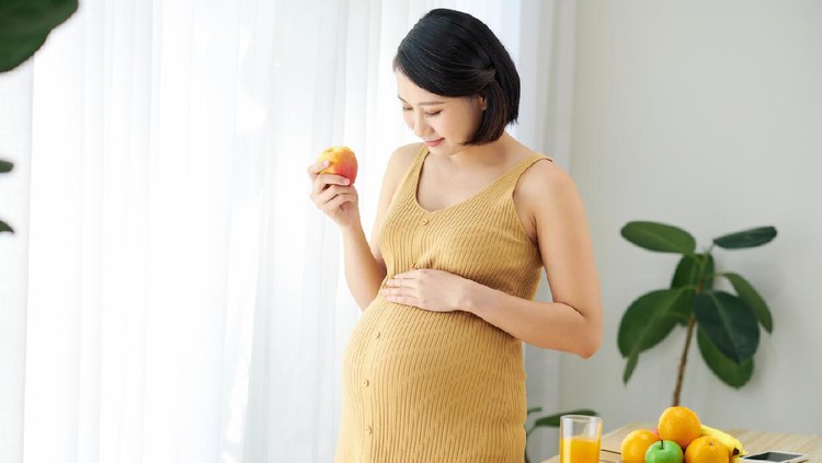 Pregnant beautiful girl holds apple, takes good care of herself by eating healthy foods.