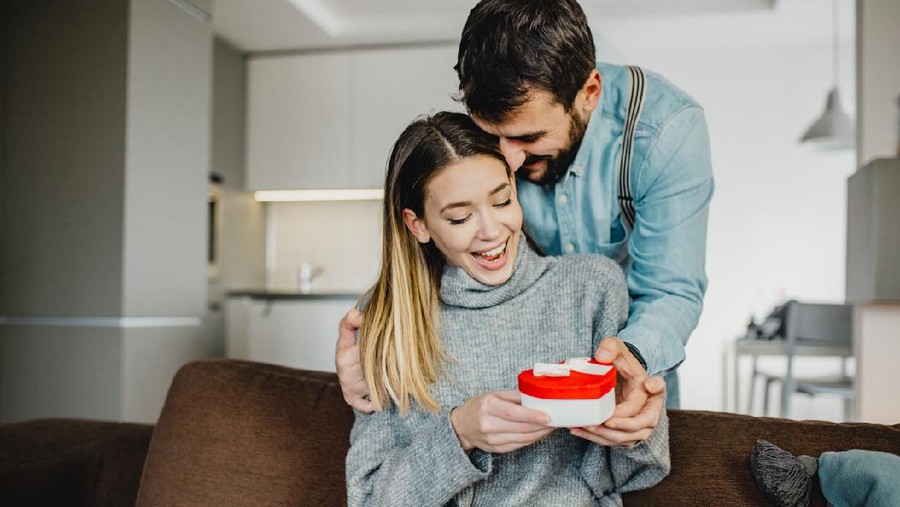 Ilustrasi Memberi Hadiah Young couple is at home. They are sitting on a couch, head to head and holding a present