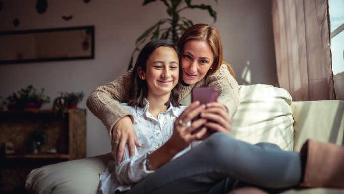 Mother and daughter sitting on a couch at home using a smartphone