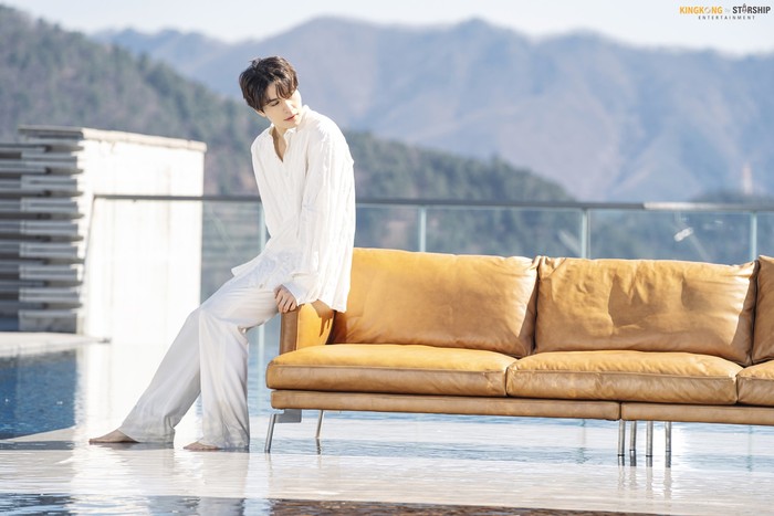 Meski mengenakan outfit polos serba putih, aktor kelahiran 6 November 1981 dengan zodiak Scorpio ini tetap memancarkan pesona yang menawan. Berlatarkan gunung, Lee Dong Wook duduk di ujung sofa coklat sambil menoleh ke arah kanan. (Foto: Naver.com/KINGKONG by Starship)