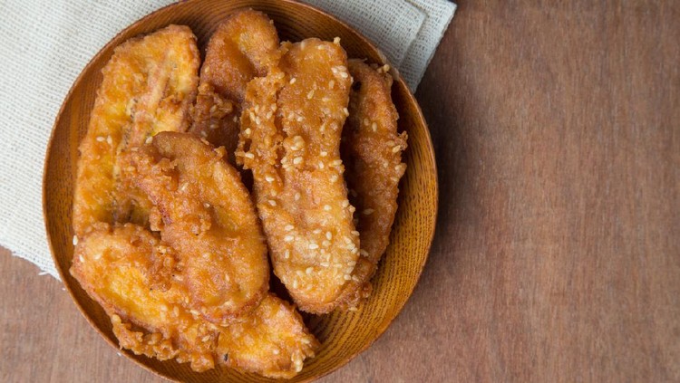 Fried bananas in wooden plate on white linen, Kluay Tod - Thai dessert.