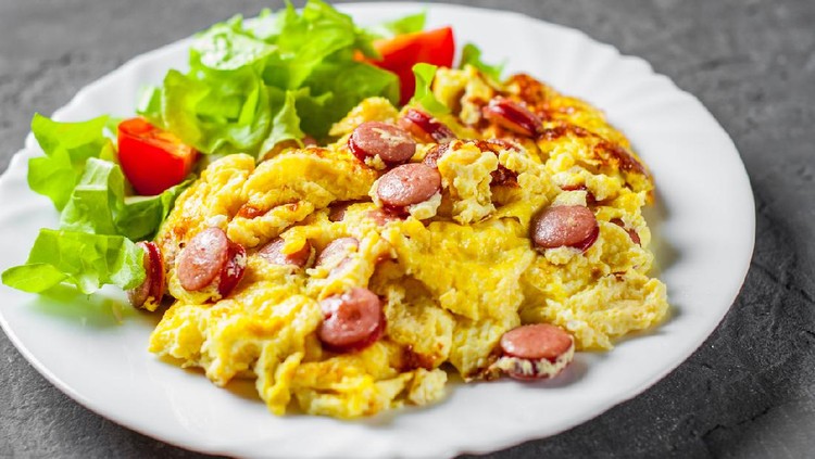 Omelet with sausage and vegetables in white plate on Dark grey black slate background