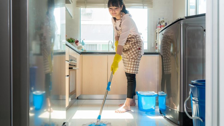 Attractive young Asian woman Mopping the kitchen floor at kitchen while doing cleaning at home during Staying at home using free time about their daily housekeeping routine.