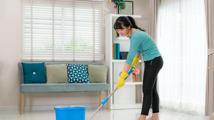 Attractive young Asian woman mopping tile floor at living room while doing cleaning at home during Staying at home using free time about their daily housekeeping routine.