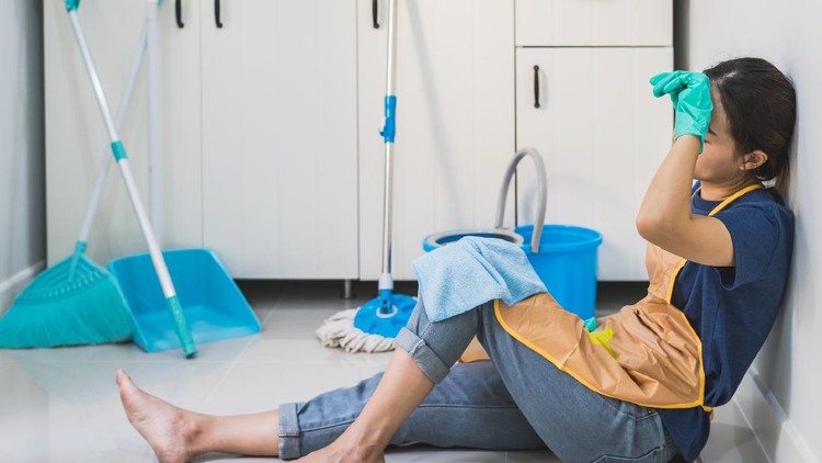 Tired young woman sitting on kitchen floor with cleaning products and equipment, Housework concept