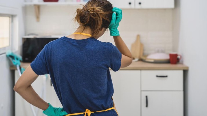 Tired young woman standing at kitchen room with cleaning products and equipment, Housework concept