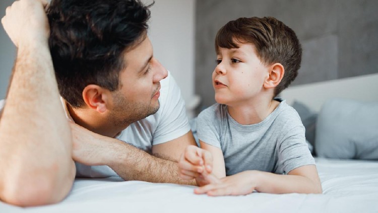 Father and his 7 years old son are talking in the bed.