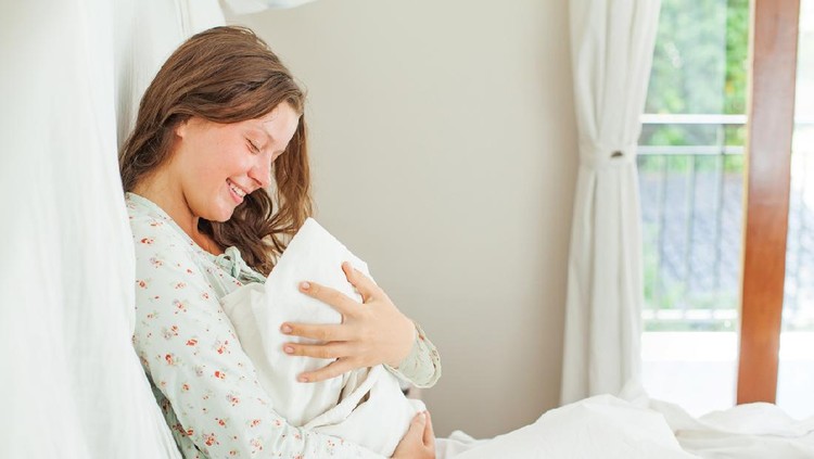 menyusui Woman sitting in a white bedroom with little child and smiling