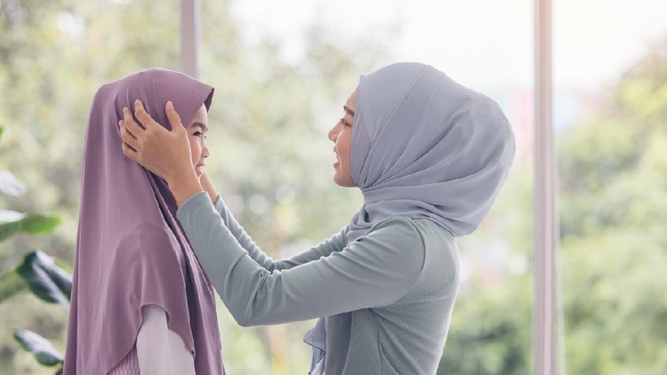 Portrait of happy lovely family arabic muslim mother and little muslim girls child with hijab dress smiling and having fun hugging and kissing together in living room
