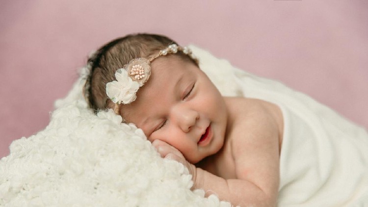 bayi perempuan Sleeping newborn baby girl laying on a cream colored blanket on a pink purple backdrop with a headband in her hair and a slight smile