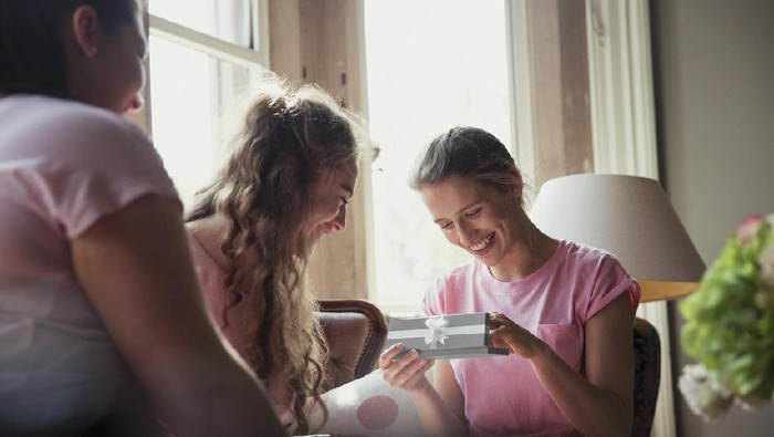 Bride her sister and friend sitting together on the morning of the bride's wedding. They are wearing matching pyjamas and the bride is opening a gift box.