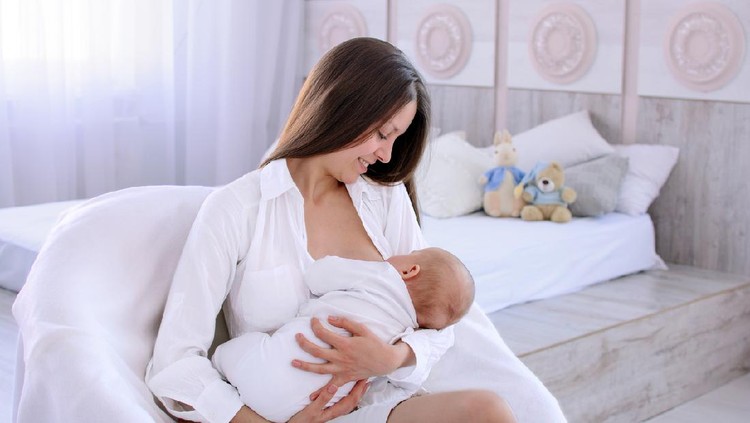 Breastfeeding baby. Young mother holding and nursing her newborn child. Woman and new born boy in white bedroom. Light interior. White clothes.
