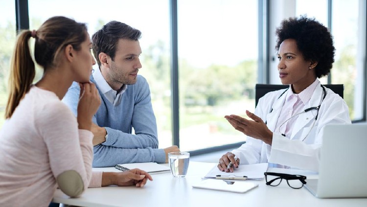 Black female doctor talking to a couple while having appointment at clinic.