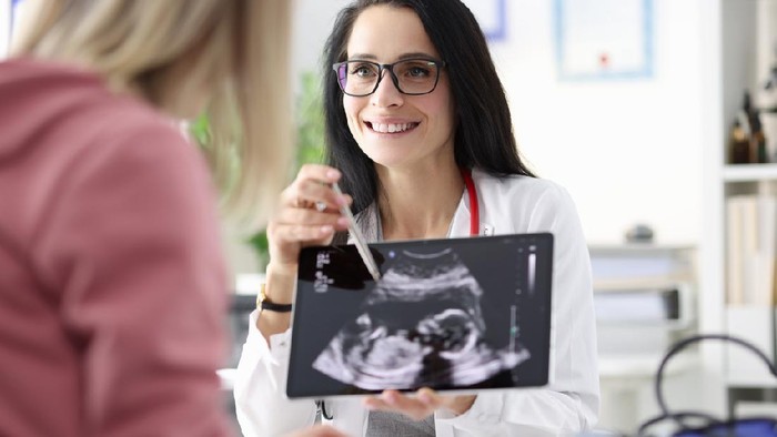 Gynecologist showing patient ultrasound of fetus on tablet. Diagnosis and management of pregnancy concept
