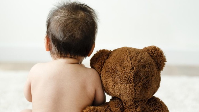A rear view photo of a mother holding her young son while they look out the living room windows.
