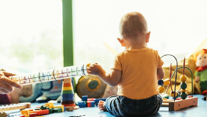 A rear view photo of a mother holding her young son while they look out the living room windows.