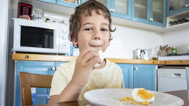 Small happy three year old boy eats an egg
