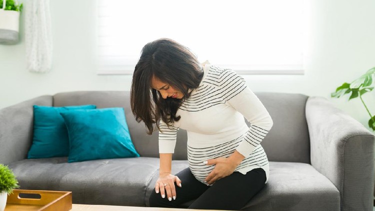 kontraksi Caucasian pregnant woman having contractions at home and about to go into a labor. Expectant mother beggining to have contractions in the sofa