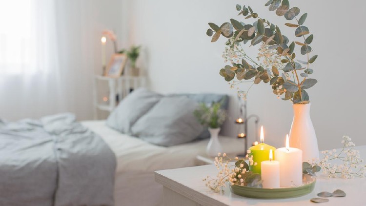 burning candles and eucalyptus in  vase in white bedroom