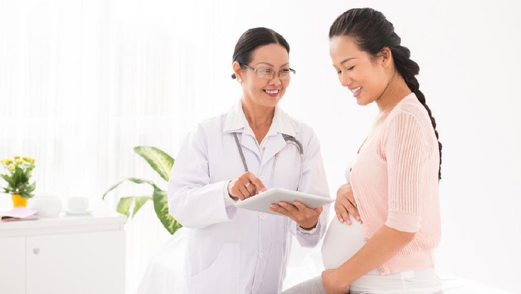 Vietnamese doctor using digital tablet at meeting with pregnant woman