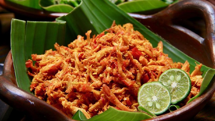 Ayam Pelalah, a common side dish in Nasi Campur Bali, is Balinese shredded chicken seasoned with spicy red chili chili paste. It is served in an earthenware cooking wok lined with banana leaf.