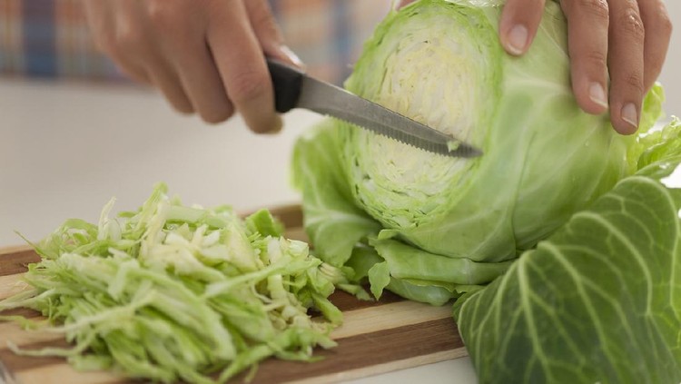 Woman cuts cabbage on cutting board in kitchen.