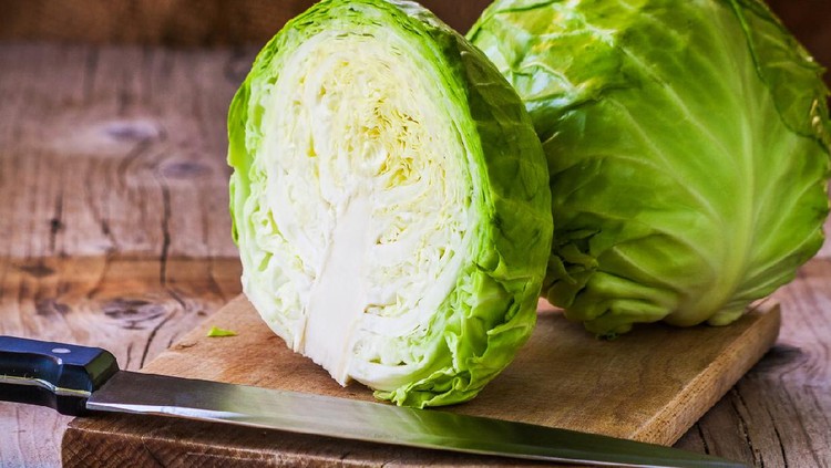 Sayur Kol Fresh green cabbage cross section with water drops on rustic wooden cutting board, kitchen knife in forground. Close up, selective focus