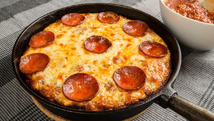 Tasty pan pizza with pepperoni salami and mozzarella in cast iron frying pan.