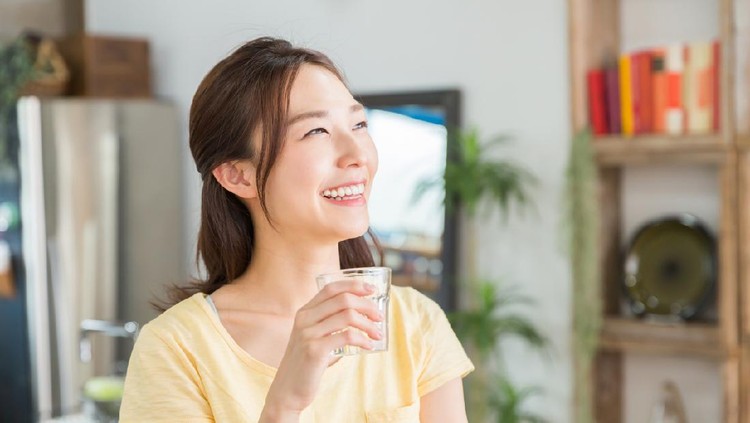 young attractive asian woman who drinks water in a kitchen