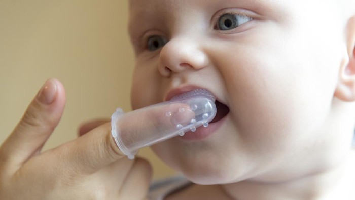 Mom brushes baby's teeth with a silicone brush that fits on her finger