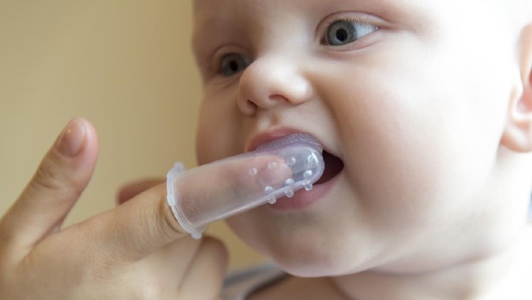 Mom brushes baby's teeth with a silicone brush that fits on her finger