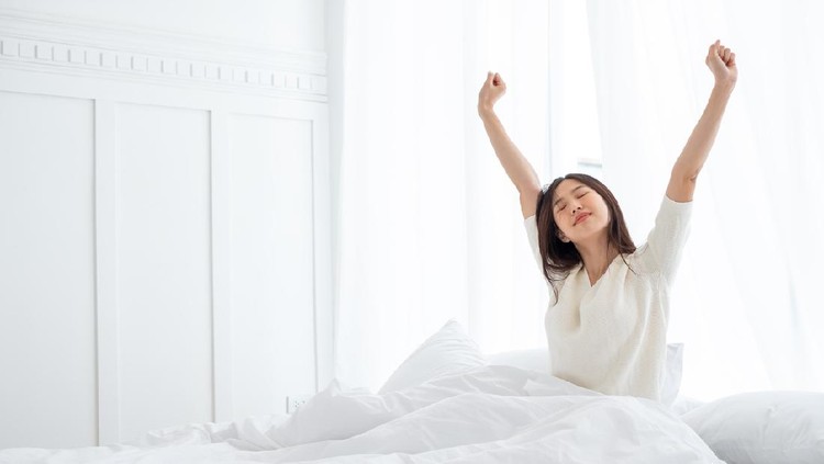 Asian woman wake up in the morning, sitting on white bed and stretching, feeling happy and fresh