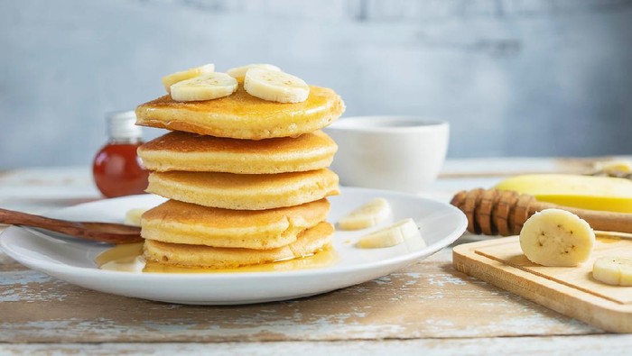 Pancakes topped with honey and bananas on the table
