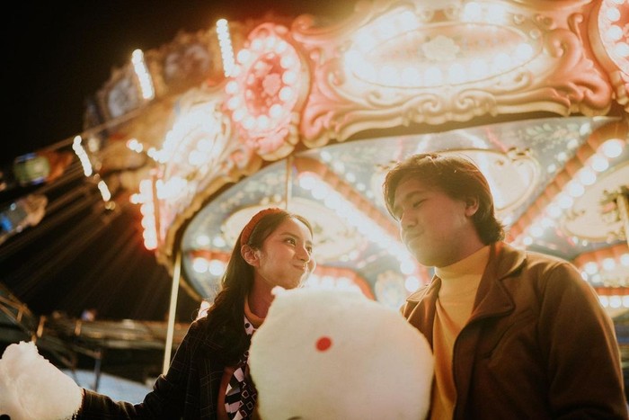 Foto prewedding tersebut dilakukan di dua tempat berbeda, yaitu Taman Wisata Bromo Tender Semeru dan Theme Park Kota Batu, Jawa Timur. Tampak dalam foto ini, keduanya berada di salah satu wahana sambil mencicipi cotton candy. (Instagram.com/jojosuherman)