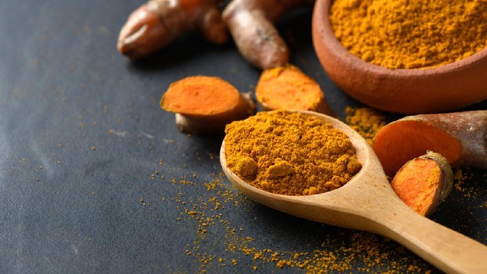 turmeric powder in wood spoon on black table, spices and herb concept