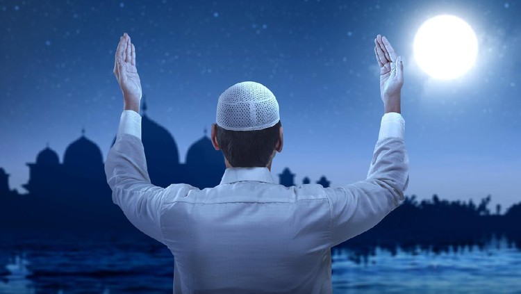 Rear view of Asian Muslim man standing while raised hands and praying with the night scene background