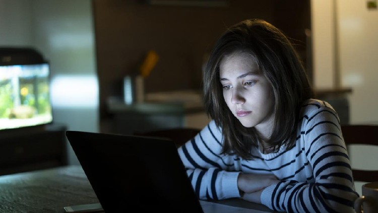 Ilustrasi cyberbullying Young girl is reading alone on her laptop late at night