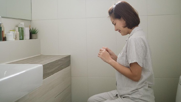 Young asian woman sitting on the bed and looking at pregnancy test in toilet in morning at home. Bangkok, Thailand.