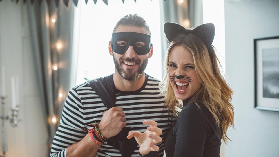 Young couple at home party celebrating Halloween in costume of thief and cat-woman