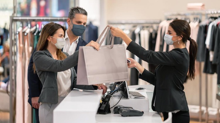 Latin American couple shopping at a clothing store and using facemasks during the pandemic while paying at the till