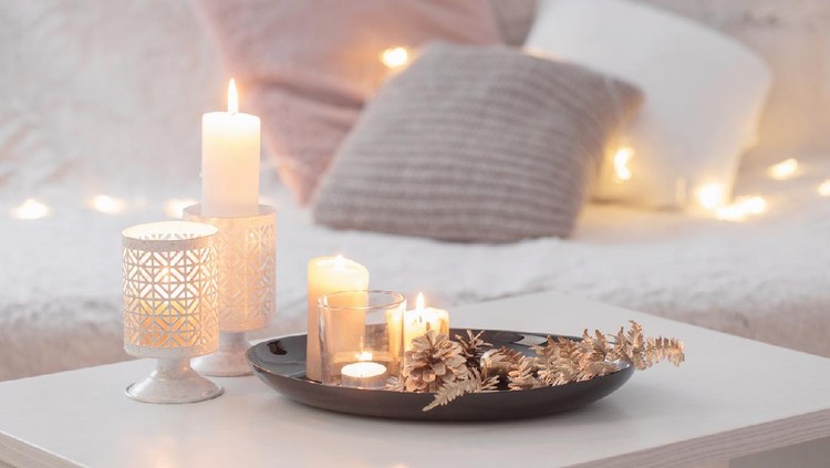 Christmas decoration   with burning candles on  white table against the background of  sofa with plaids and pillows. Cozy home and holiday concept