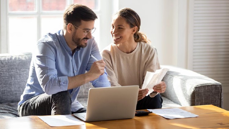 Ilustrasi Menabung Bersama Suami Happy young married couple sit on couch calculate expenses use easy online banking service at home, smiling millennial husband and wife count taxes house expenditures pay bills on internet