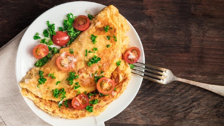 A photo of an omelette with cherry tomatoes, parsley. and grated cheese, shot from above on a rustic wooden texture with a place for text