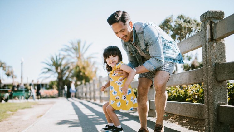 A dad helps his little girl go skateboarding, holding her waist for support.  Shot in Los Angeles, California by the Santa Monica Pier.
