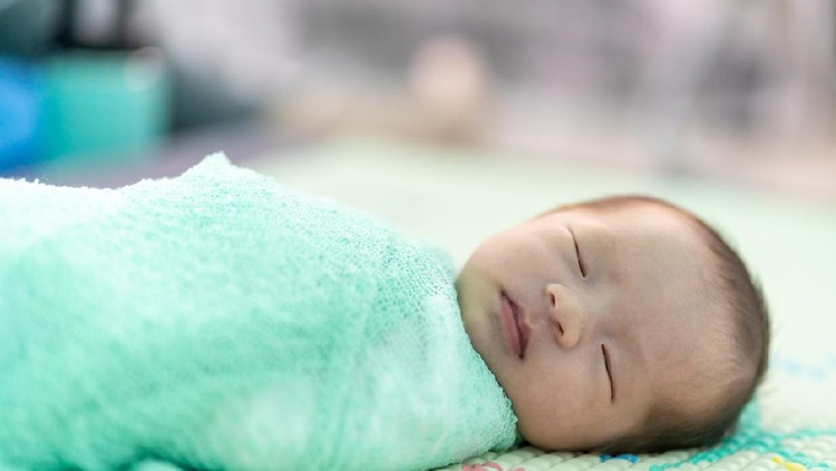 The newborn was wrapped in a green cloth and was placed on a soft rubber mat with a blurred background.