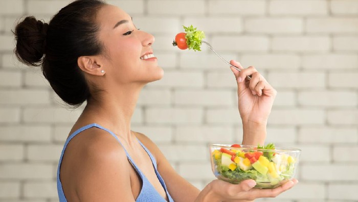 Asian woman in joyful postures with hand holding salad bowl