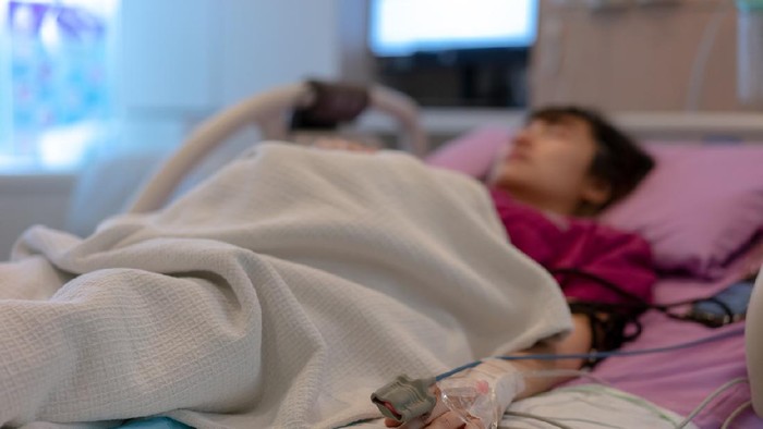 Asian female patient warded and laying on the bed connected to multiple medical devices